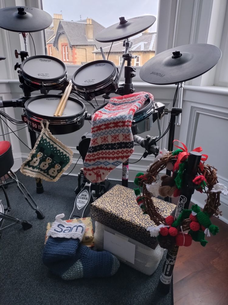 An electronic drumkit with a Christmas wreath hanging off it, and presents and stockings underneath