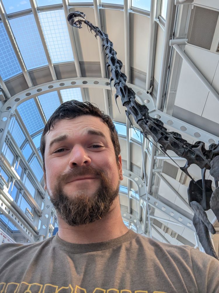 Selfie photo of me in front of O'Hare Airport's replica Brachiosaurus skeleton