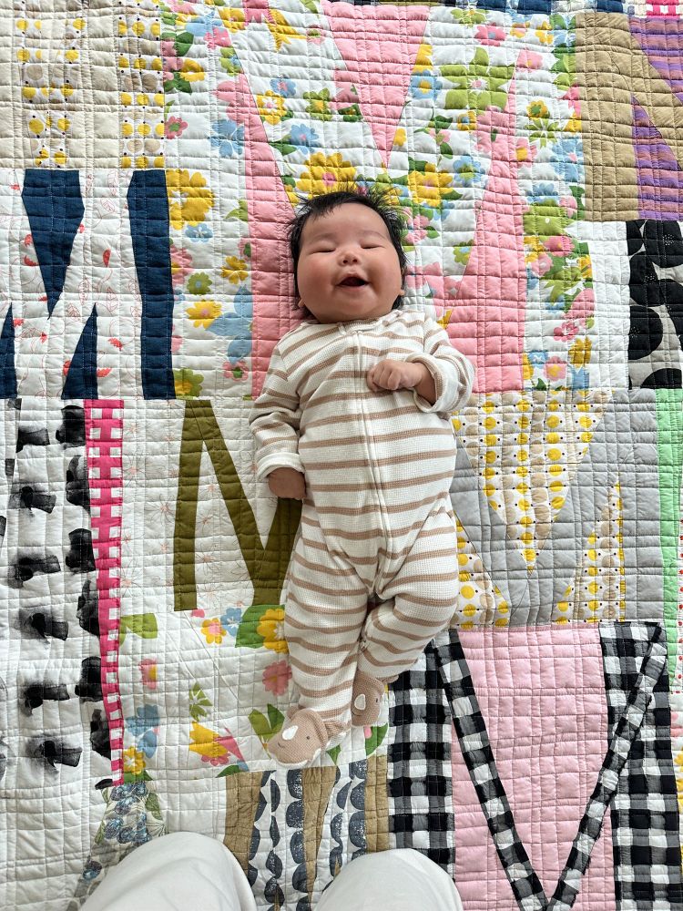 Newborn baby lying on a baby quilt with improv Ms