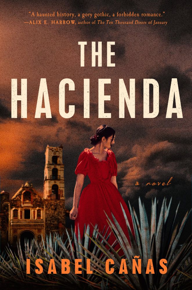Cover for The Hacienda by Isabel Cañas. Young woman facing to the right with dark hair in a loose bun in a long red dress among plants, in the background is a large house.