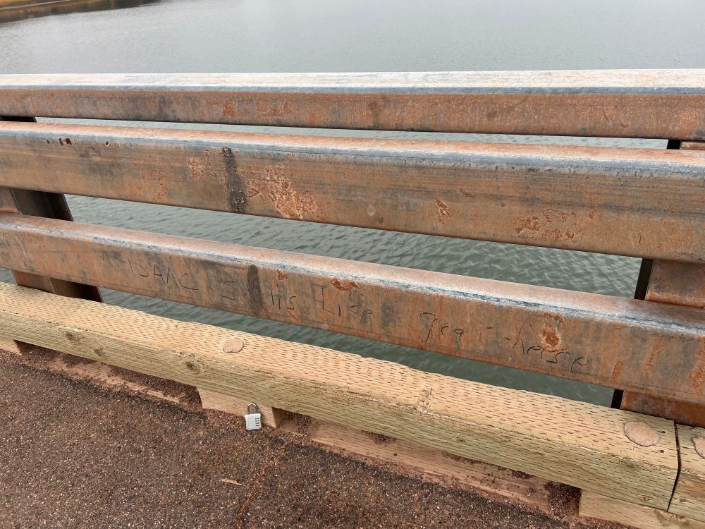 graffiti on a bridge rail that says “Isaac smells like great cheese”