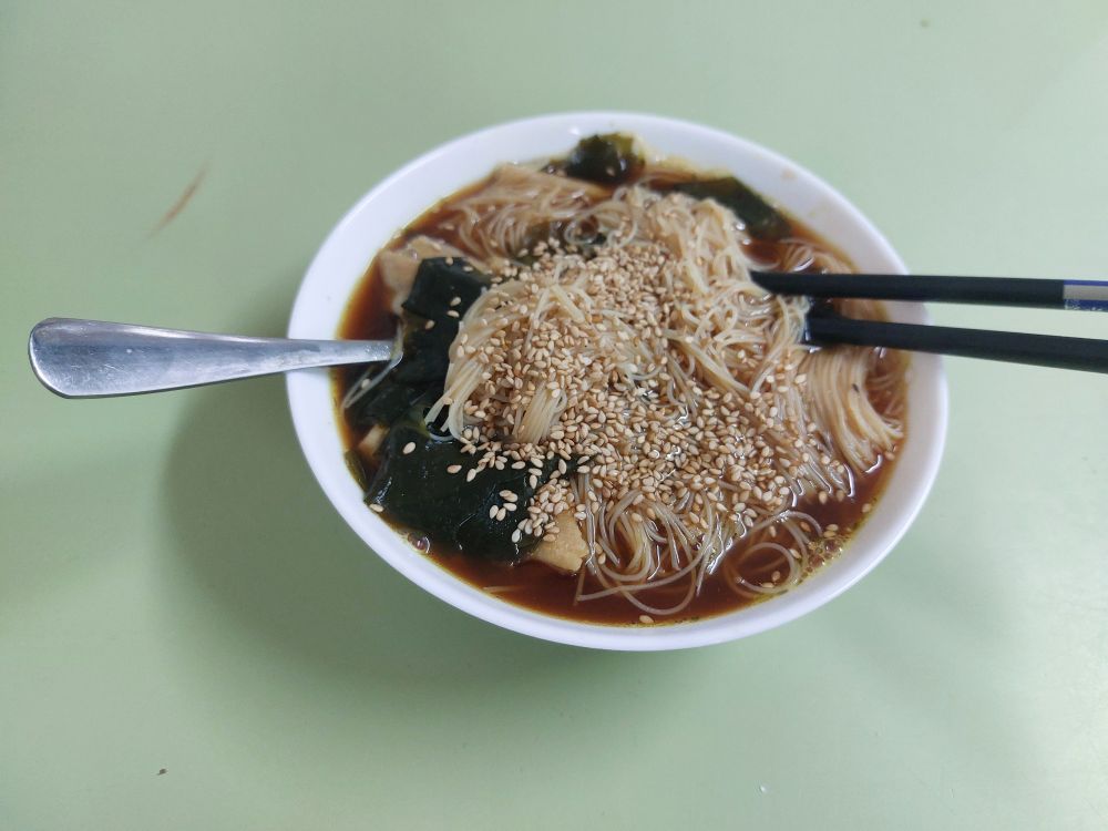 a bowl of brown seaweed soup with vermicelli rice noodles and sesame seeds