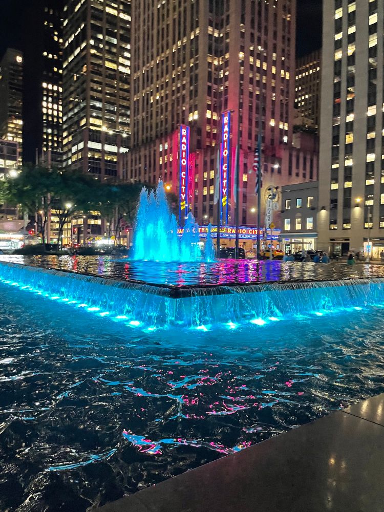 Rockefeller Center fountain at night with Radio City Hall in the distance; August 28, 2025