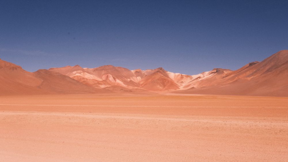 Dalì Desert in Bolivia, beige and Brown scenery with mountains in the back sprinkled with white sand. 