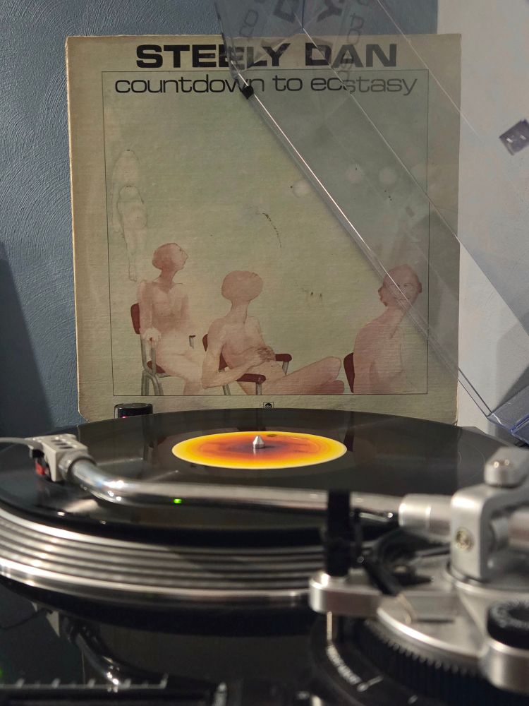 Side view of a black AT-LP120 spinning Countdown to Ecstasy by Steely Dan, its jacket propped up against the dust cover in the background 