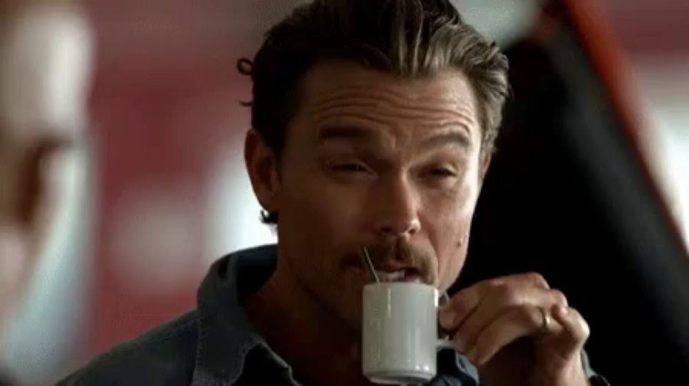 a man with a mustache is drinking coffee from a white cup .