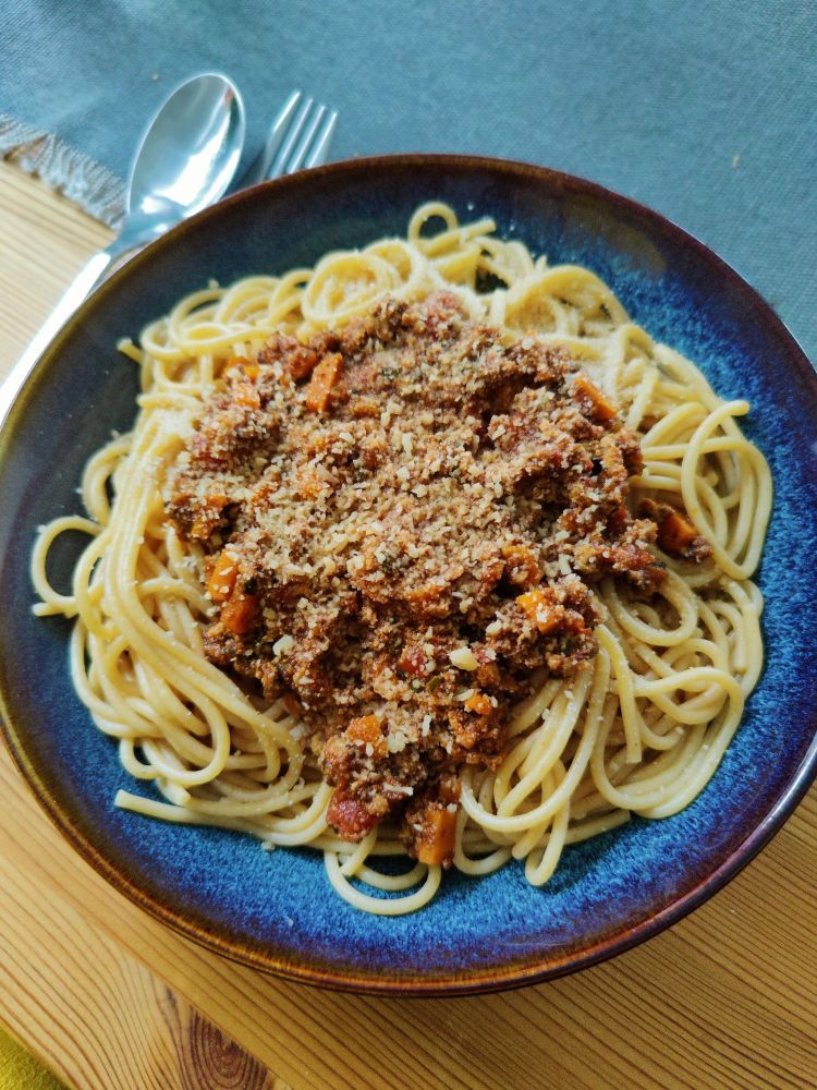 Blauer Teller mit einer Portion Nudeln und Tofubolognese, bestreut mit Parmesan