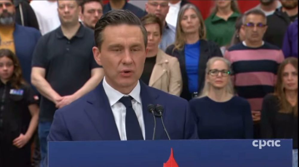 Pierre Poillievre getting ready to vomit more bullshit at a lectern. The tiny group behind him is designed to look both closer than they really are and more populous by far than it was