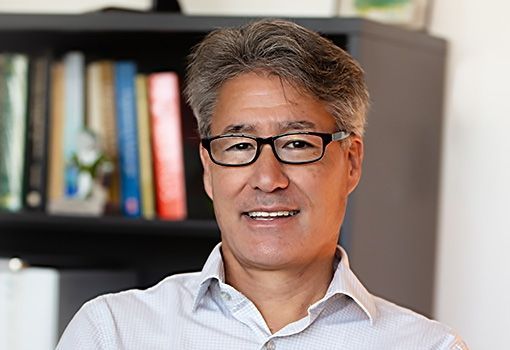 Jeff Sakamoto smiling and standing in front of a bookcase