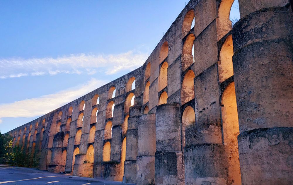 The sun dips low on the horizon, casting a golden glow upon the ancient stones of the Amoreira Aqueduct in Évora, Portugal. Its elegant arches, a testament to Roman engineering, stretch across the landscape, carrying the echoes of a bygone era.
The weathered stones, bathed in the warm light, reveal the passage of time, each crevice whispering stories of centuries past. The aqueduct stands as a silent sentinel, a witness to the rise and fall of civilizations.
A simple road runs alongside, a stark contrast between the ancient structure and modern life. The sky above, a canvas of soft hues, mirrors the tranquility of the scene.
In the distance, the city of Évora rests, its own history intertwined with the aqueduct's legacy. Together, they form a timeless tableau, a reminder of the enduring power of human ingenuity and the beauty of the past.
