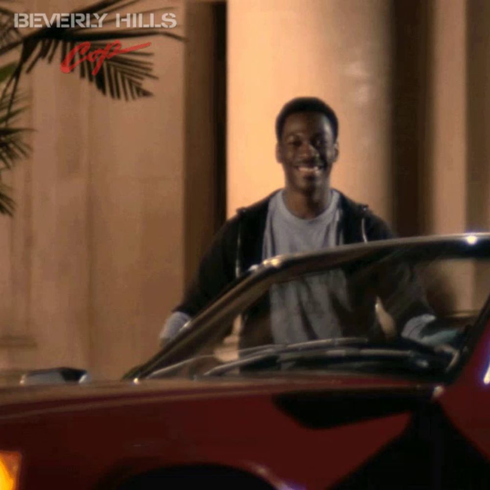 a man standing next to a red car with beverly hills written on the bottom