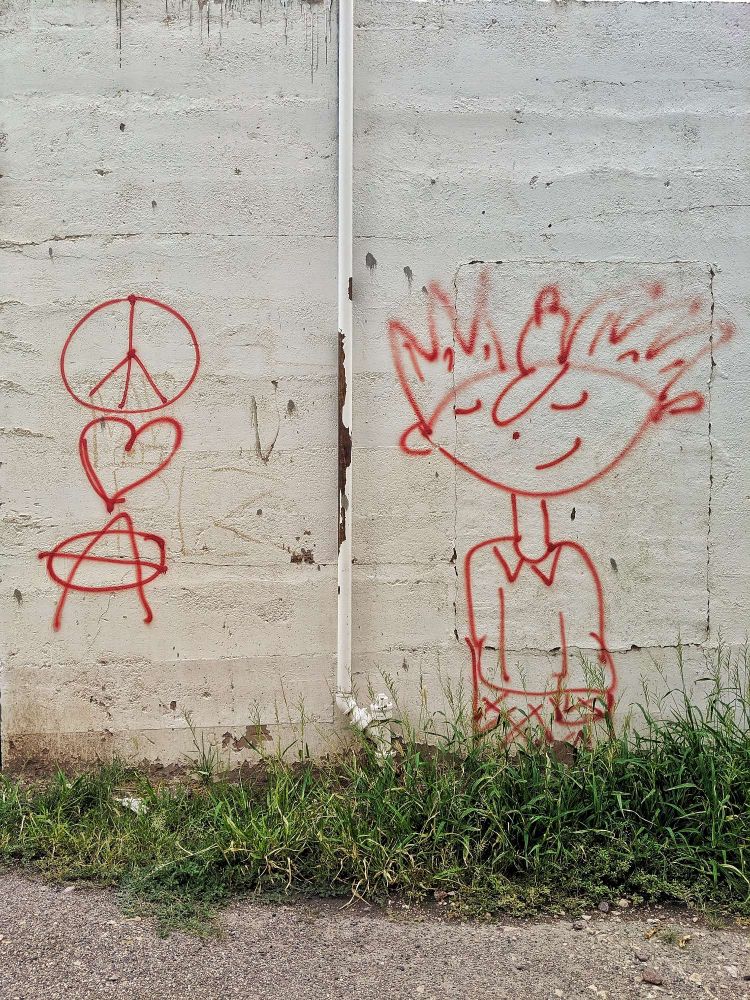 Street graffiti of peace, love, and anarchy symbols next to another graffiti of Arnold from Hey Arnold.