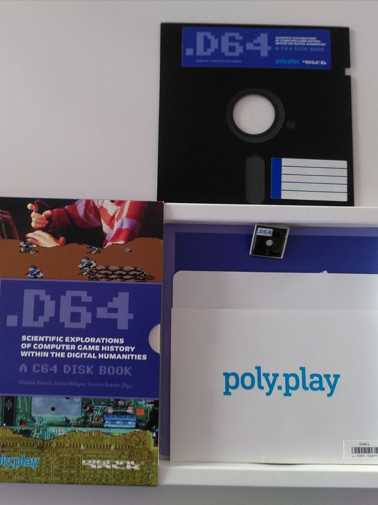 Der Inhalt einer kleinen Kartonschachtel ist abgebildet. Es handelt sich um die Publikation:
.D64. Scientific Explorations of Contemporary History Within The Digital Humanities: A C64 Disk Book.

Herausgegeben haben es Melanie Fritsch et al.

Die Schachtel mit quadratischer Grundfläche liegt geöffnet auf einem Tisch. In der Schachtel liegt eine Hülle aus Papier mit der Aufschrift "poly.play" und der Zugangsnummer der Deutschen Nationalbibliothek. Außerdem befindet sich ein Button im Inneren, der aussieht wie eine kleine Diskette mit der Aufschrift C64. 
Auf dem Bild oberhalb der Schachtel liegt eine Diskette, die in einem C64 Homecomputer abgespielt werden kann. Das Buch ist auf dieser Diskette gespeichert. Es kann aber auch über einen QR Code heruntergeladen werden, den ich vorsichtshalber nicht  fotografiert habe.