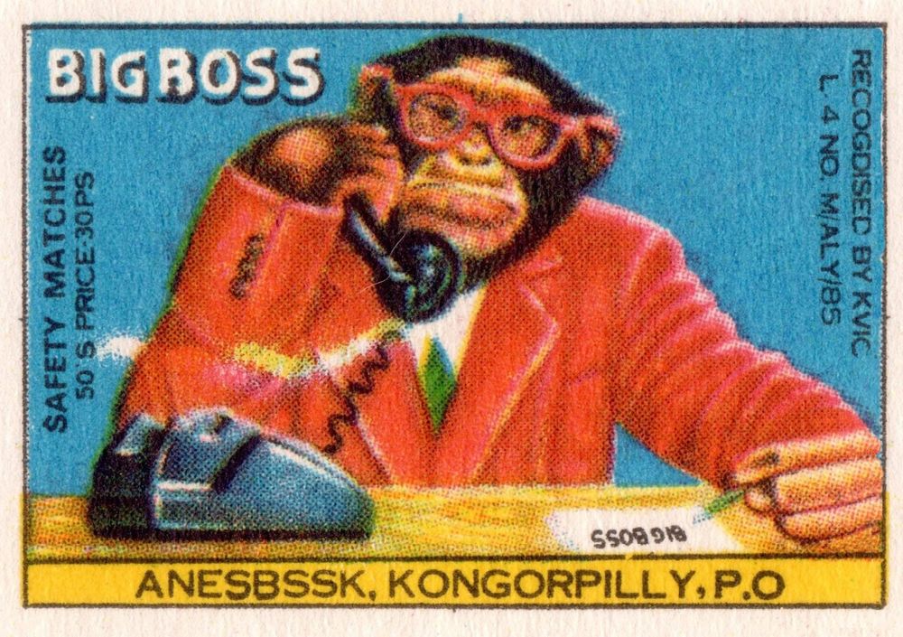 Matchbox cover for Big Boss safety matches (from Kongorpilly, a village located in the Ernakulam district of Kerala, India), featuring a painting of a monkey in a suit tsitting at a desk and talking on a telephone.