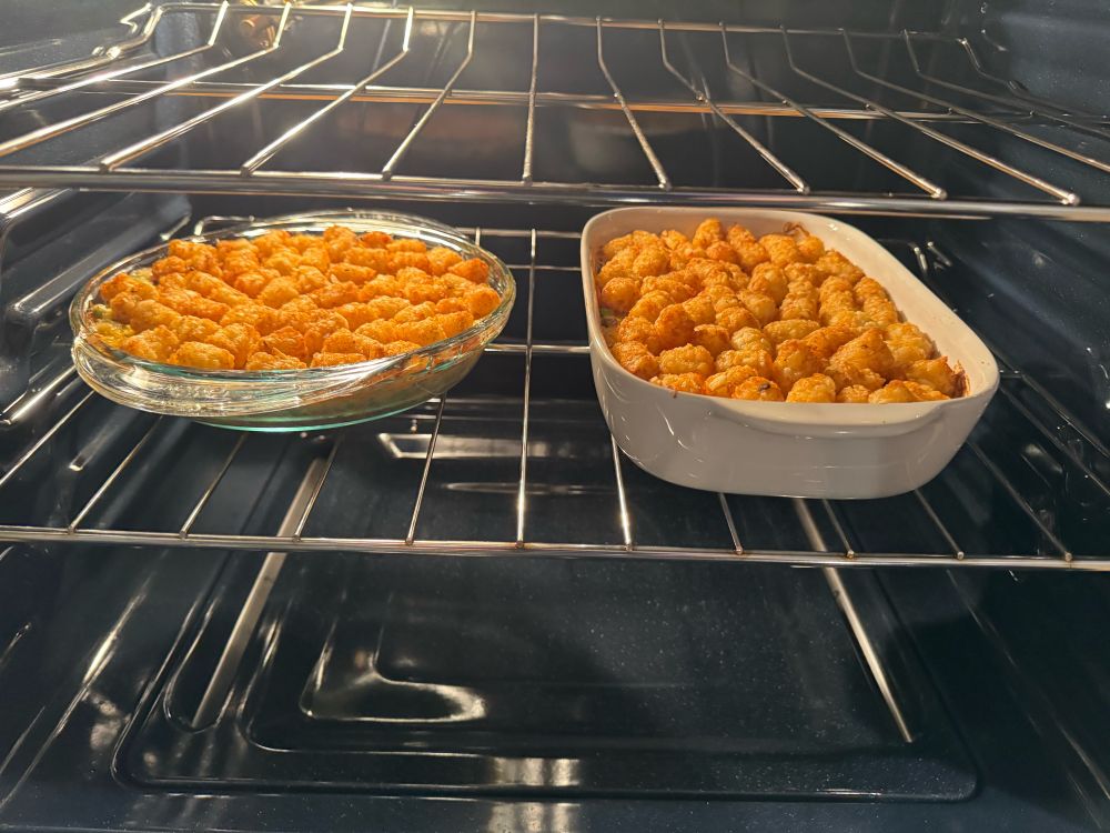 Two casserole dishes topped evenly with tater tots baking in an oven.