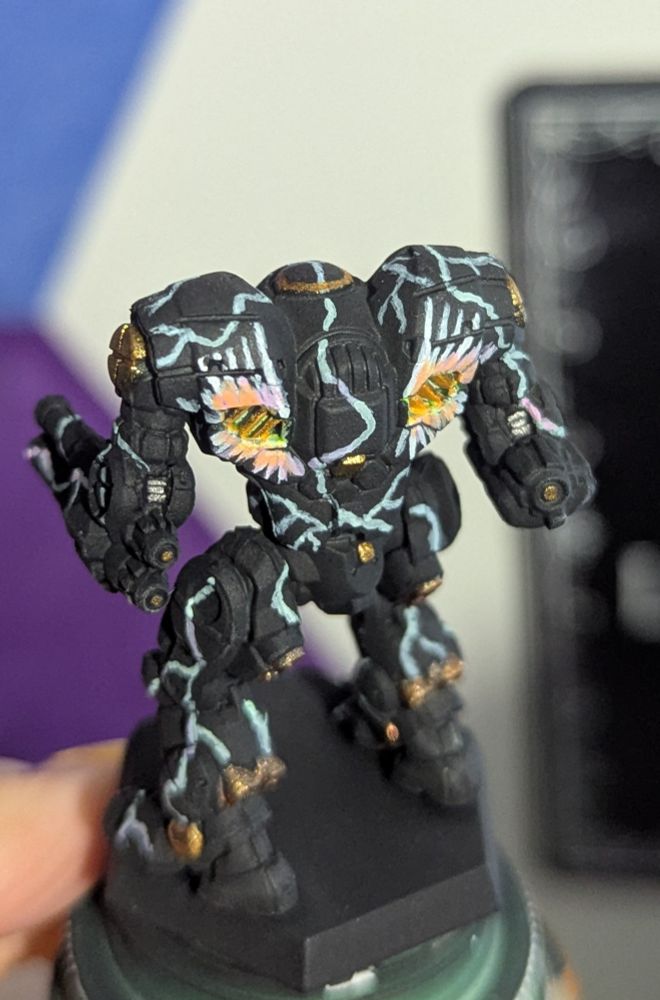 A close up rear shot of a Battletech miniature painted black with gold accents, streaks of lightning, glowing wings and a halo.