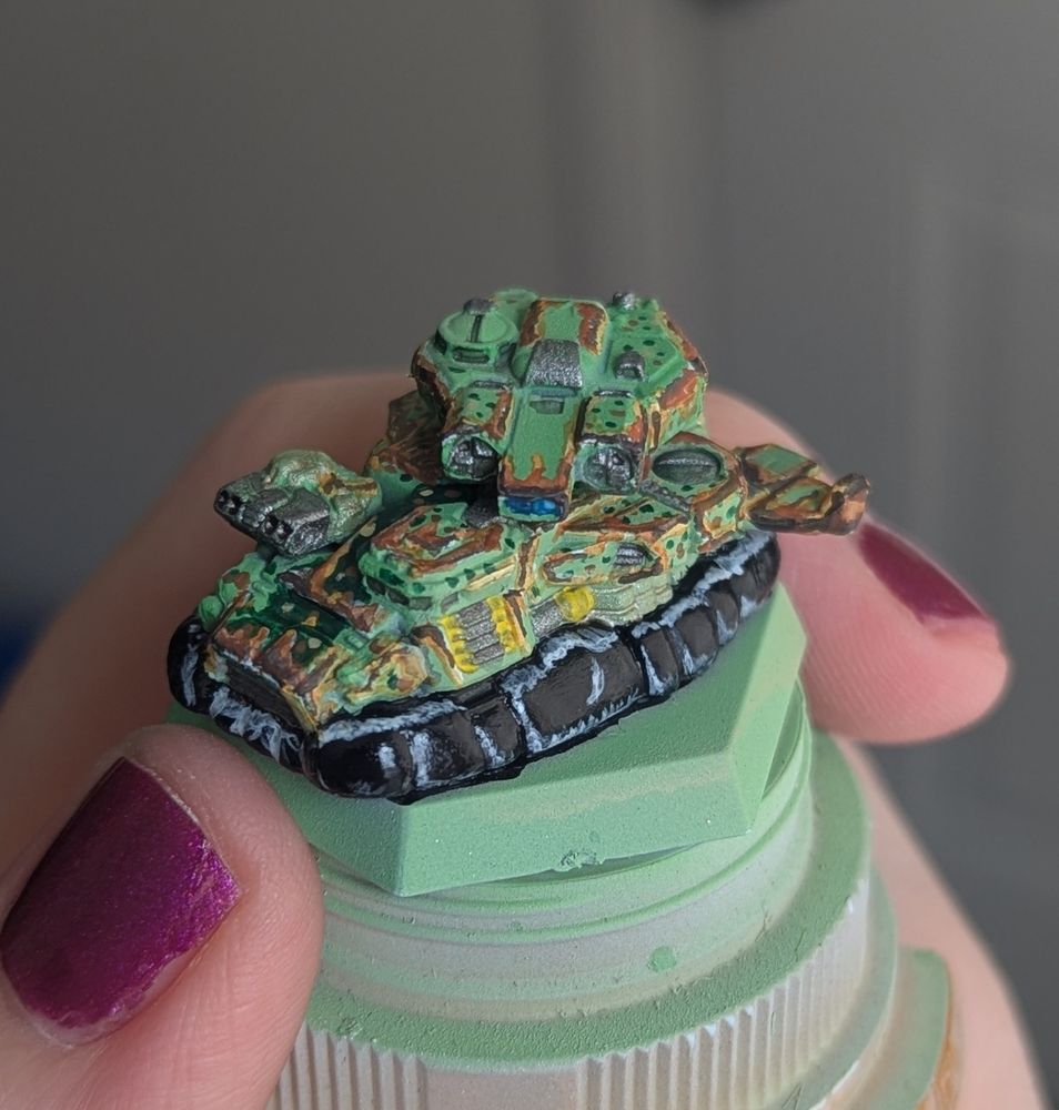 A miniature Drillson hover tank from the Battletech tabletop wargame, painted in green and brown camouflage with heavy rust and streaking.