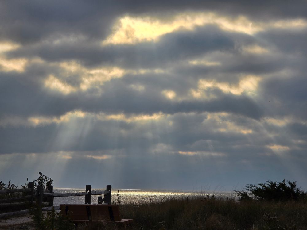Sun breaking through dark clouds over the bay with visible rays and brilliance on the water far away. 