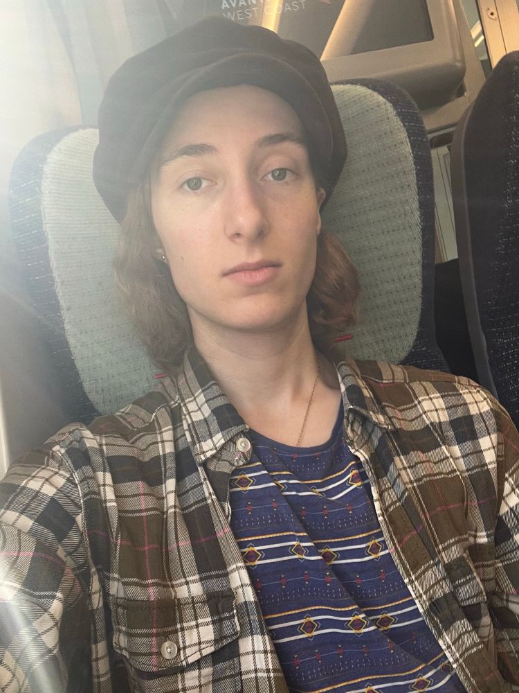 Tired twink in a flat cap sitting on a train 
