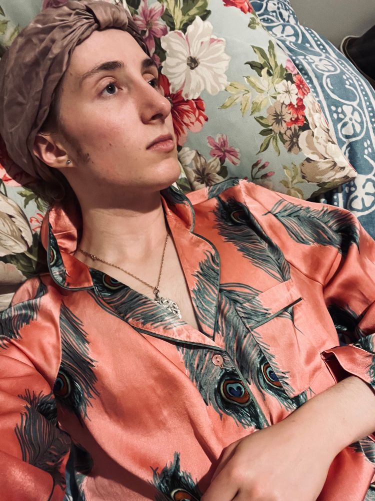 Twink, wearing silk pyjama and a purple hair bonnet, laying in bed and staring into the distance 
