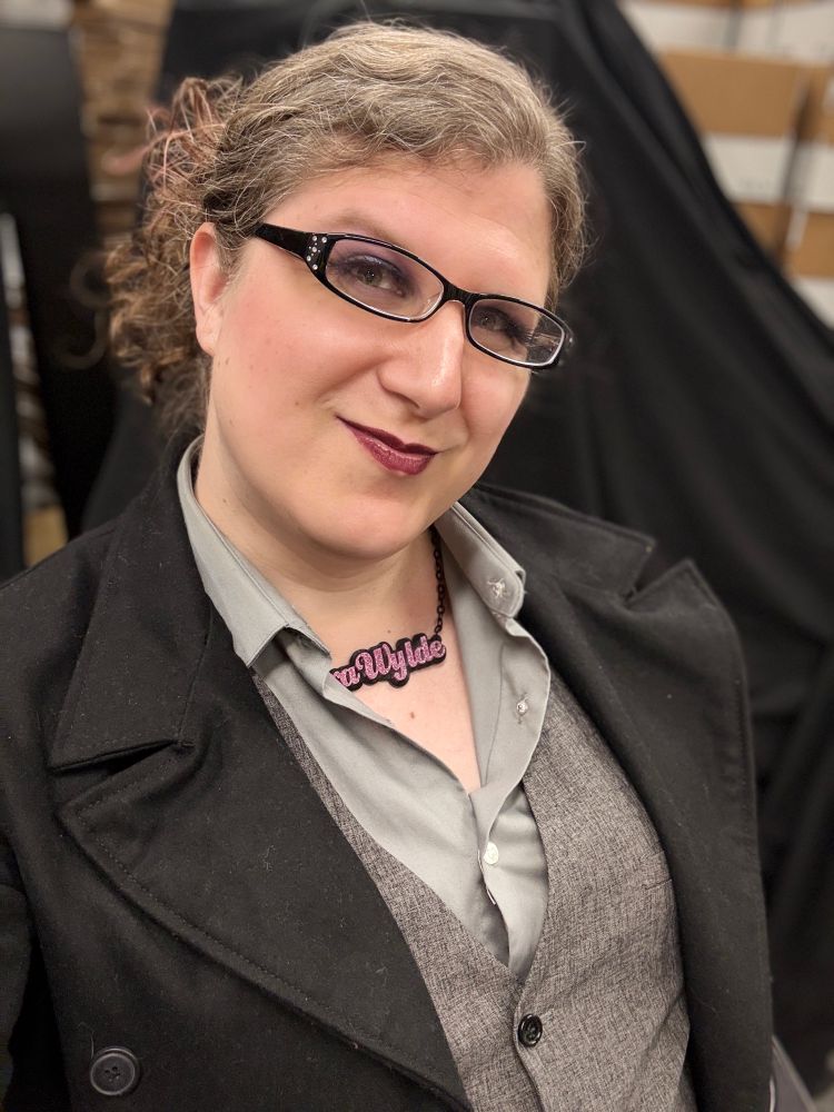 Vera with her hair pulled back in a jacket, vest? And button down shirt. 