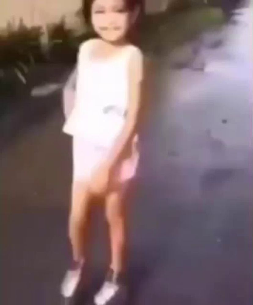 a little girl in a white dress and white sneakers is standing on a skateboard .