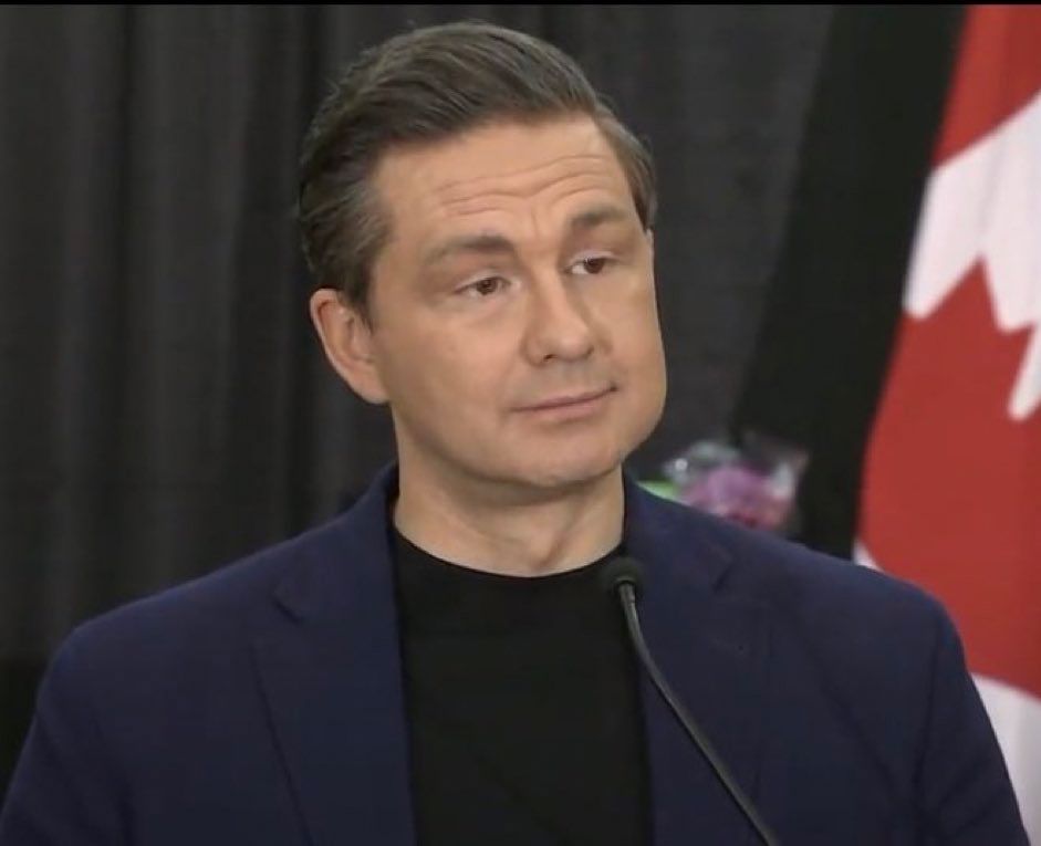 Pierre Poilievre in a dark navy suit and black shirt next to a Canadian flag 