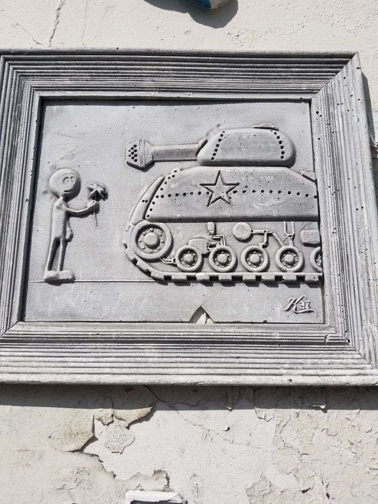 Petit bonhomme tout mignon seul devant un tank façon Tien-en-Men, qui tient un bouquet de fleurs