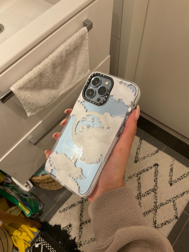 An iPhone with a clear MagSafe case with clouds, by casetify, angled to show how it reflects light. 