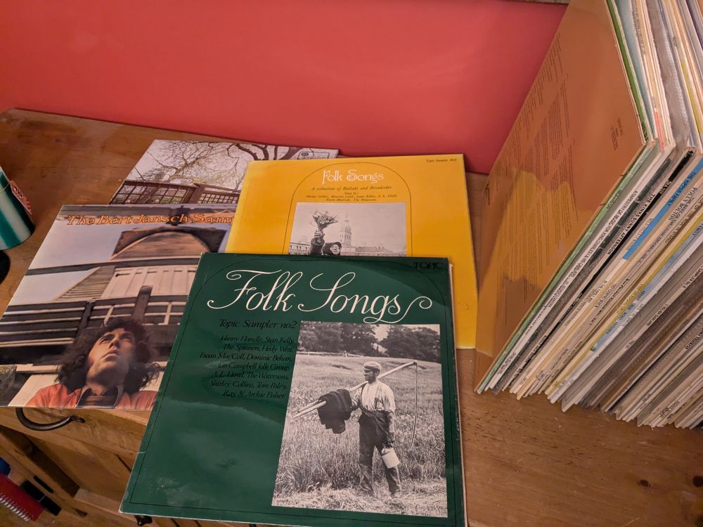 Old LP vinyl records on a wooden surface. Four records are laid out flat, they are a Bert Jansch sampler, two Topic Folk Samplers, and Fairport Convention's Unhalfbricking.