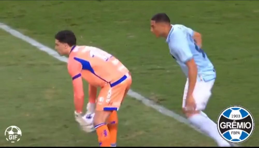 Carlos Vinicius from Grêmio lurks behind Brenno, the goalkeeper from Fortaleza, who is about to put down the ball. Vinicius quickly steals it and scores in an open goal.