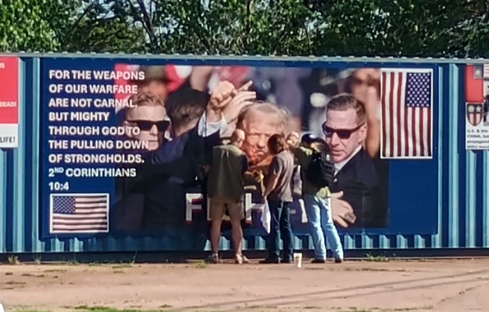 A mural of Trump with the word fight underneath. Three guys are standing in front trying to remove the word PEDO that was spray painted.