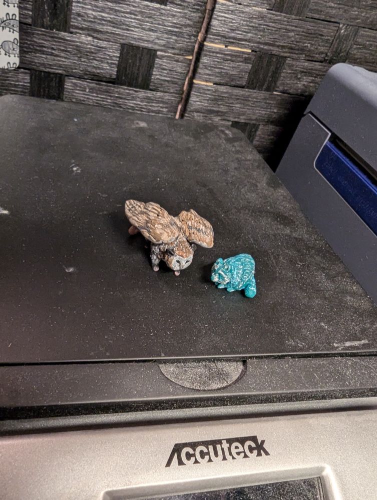 Two tiny sculptures made with Sculpy clay of an opossum with the wings and face of an owl, and a blueish-green raccoon. Slightly higher angle than first photo.