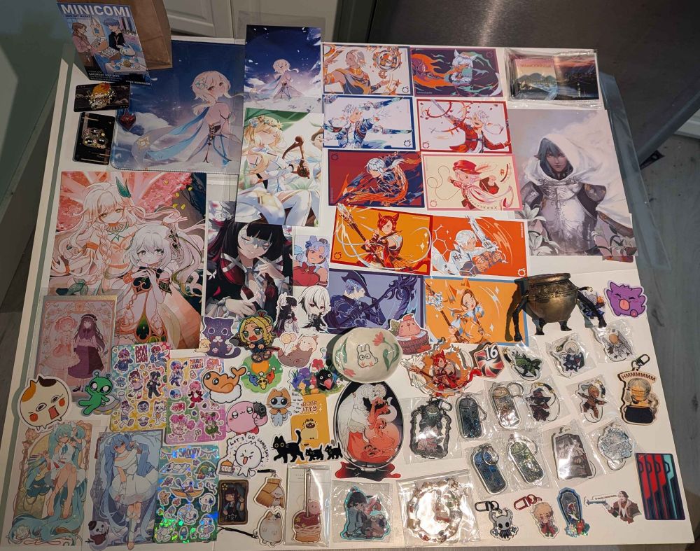 A white dinner table covered in various art prints, stickers, charms, and even a ceramic and a figure! 