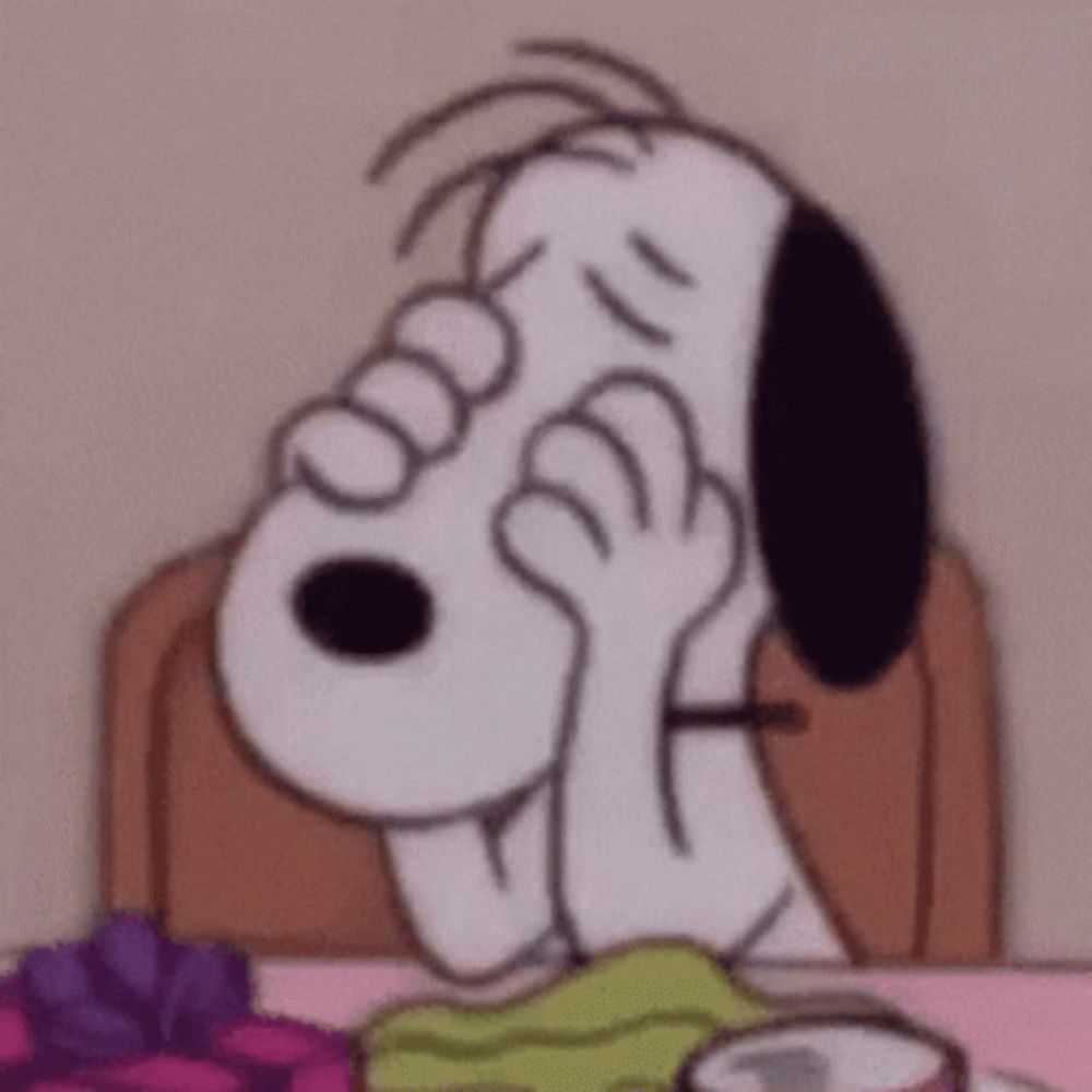 snoopy is covering his face with his hands while sitting at a table with presents .