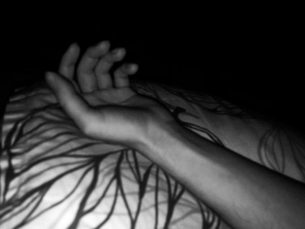 A black and white photo of a hand resting on a pillow, lighted by a flash in an otherwise dark bedroom.