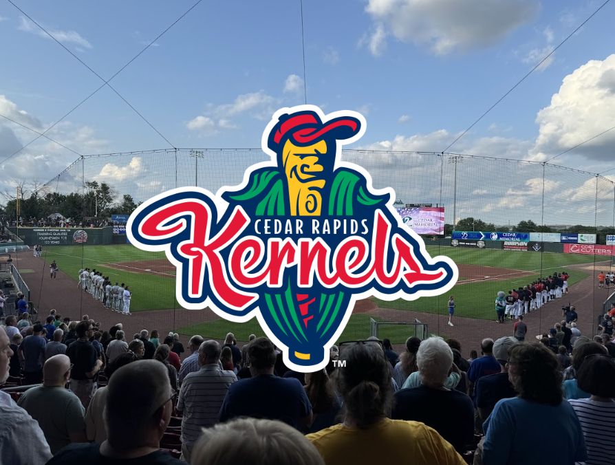 A Cedar Rapids Kernels logo in front of a photo of the Kernels game we attended in 2024