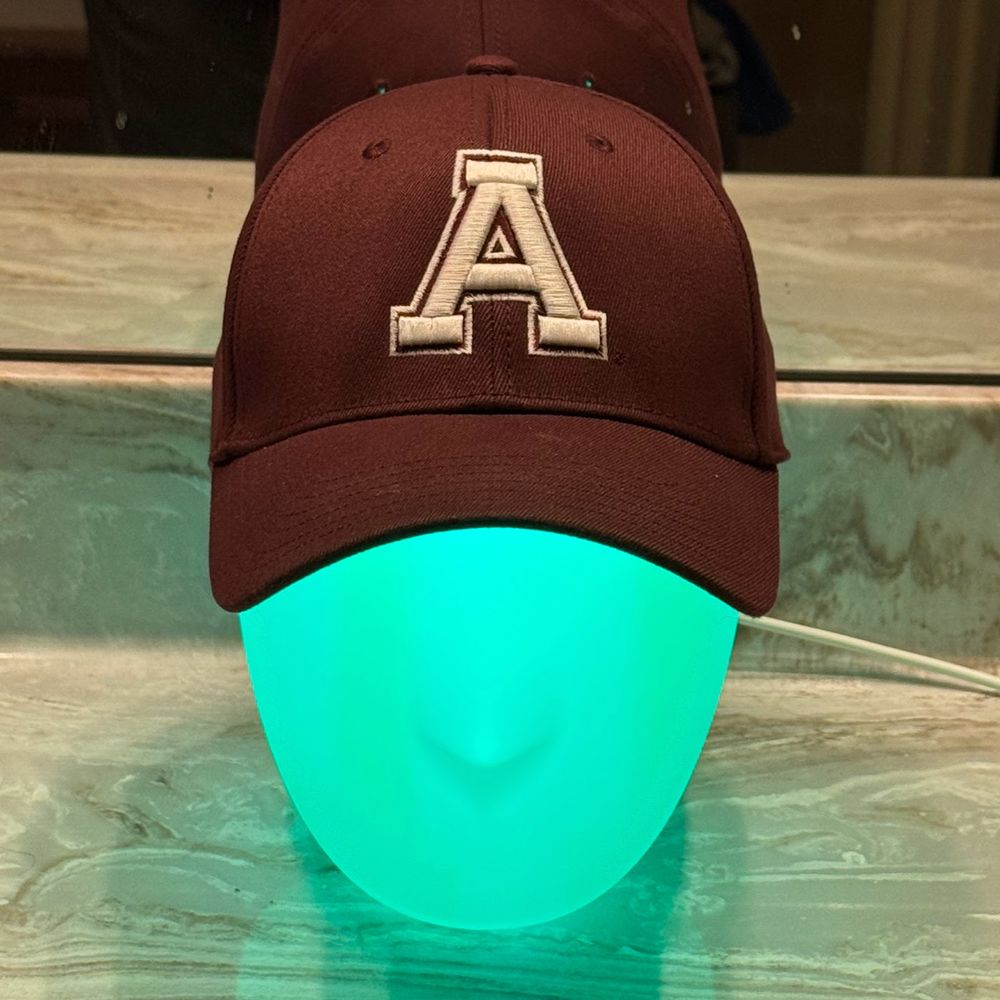 Thomas MacHeadison is glowing teal and wearing a maroon and cream Alma Scots baseball cap