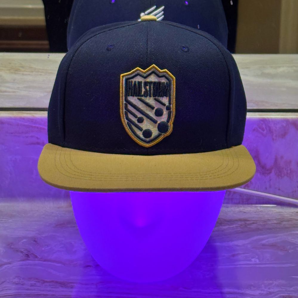 Thomas Headison is glowing purple and wearing a navy and light gold Northern Colorado Hailstorm FC baseball cap
