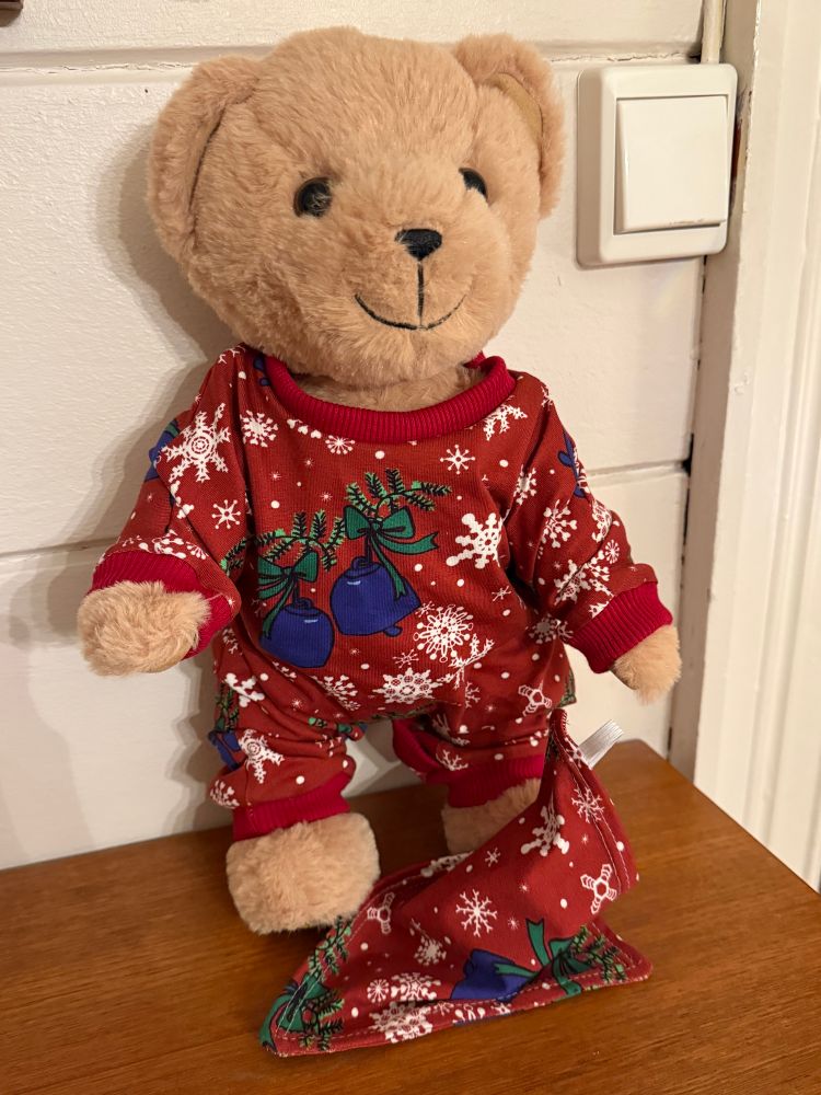 En bamse som har på seg en rød pysjamas med snøfnugg og bjeller. 