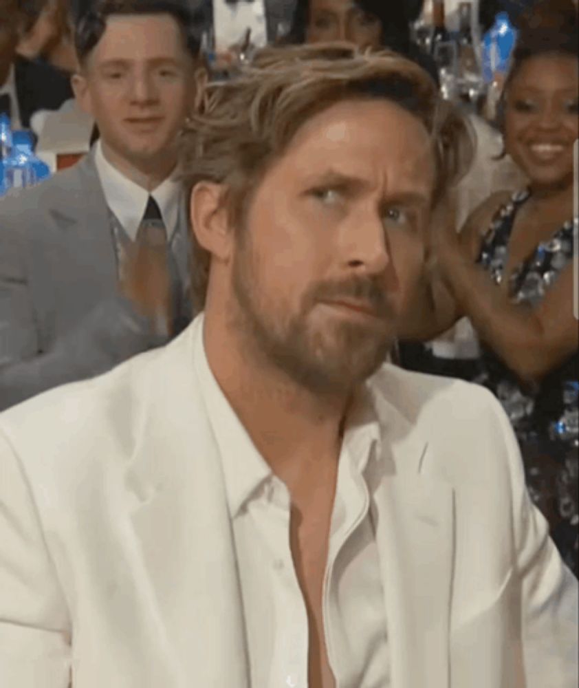 a man with a beard wearing a white suit looks at the camera