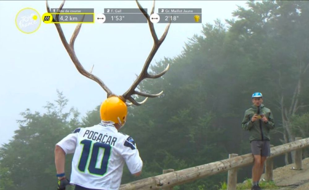 A man in a Tadej Pogacar Seattle Seahawks jersey is running up a hill at the Tour de France and wearing a helmet with huge antlers