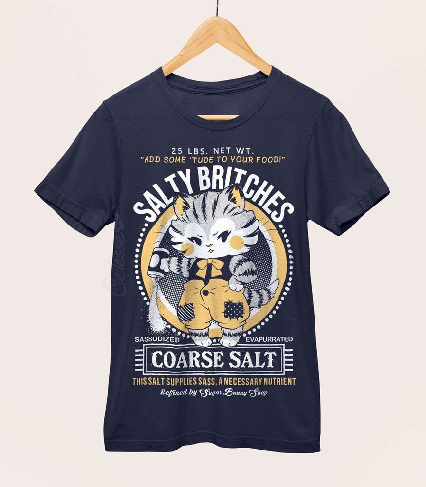 A photo of a navy blue shirt on a wood hanger, the printed design features a vintage-style logo for Salty Britches Coarse Salt with a kitten wearing patchwork britches and petulantly pouring out a container of salt.
