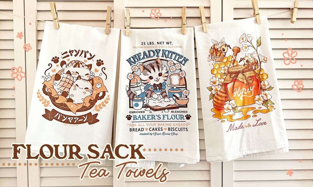 A photo of three flour sack tea towels hung on a line with clothes pins, set in front of a beige slatwall door. The printed images featured are of a bakery logo with 3 bread cats, a logo for Kneady Kitten Baker's Flour, and a jar of honey with pretty bees flying around. The text reads, "Flour Sack Tea Towels."