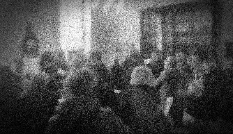 A room with furniture, display boards, and quite a lot of people.