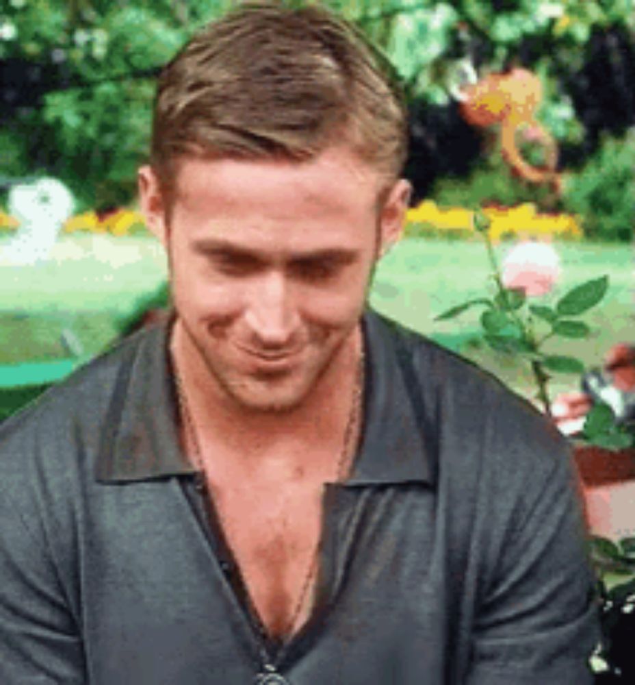 a man with a necklace around his neck is smiling while sitting in front of a flower pot .