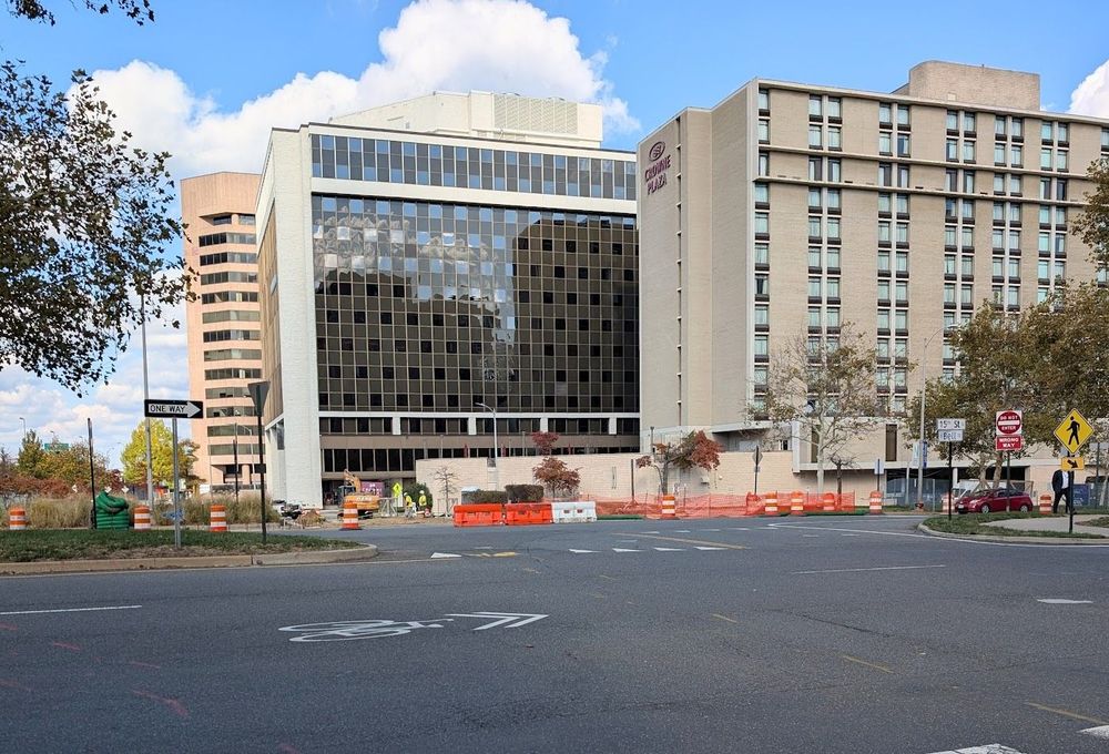 The intersection of 15th St S and S Bell St in Crystal City. Orange construction barriers and fencing can be seen on the other side of the intersection. There are mid/high-rise buildings in the background.
