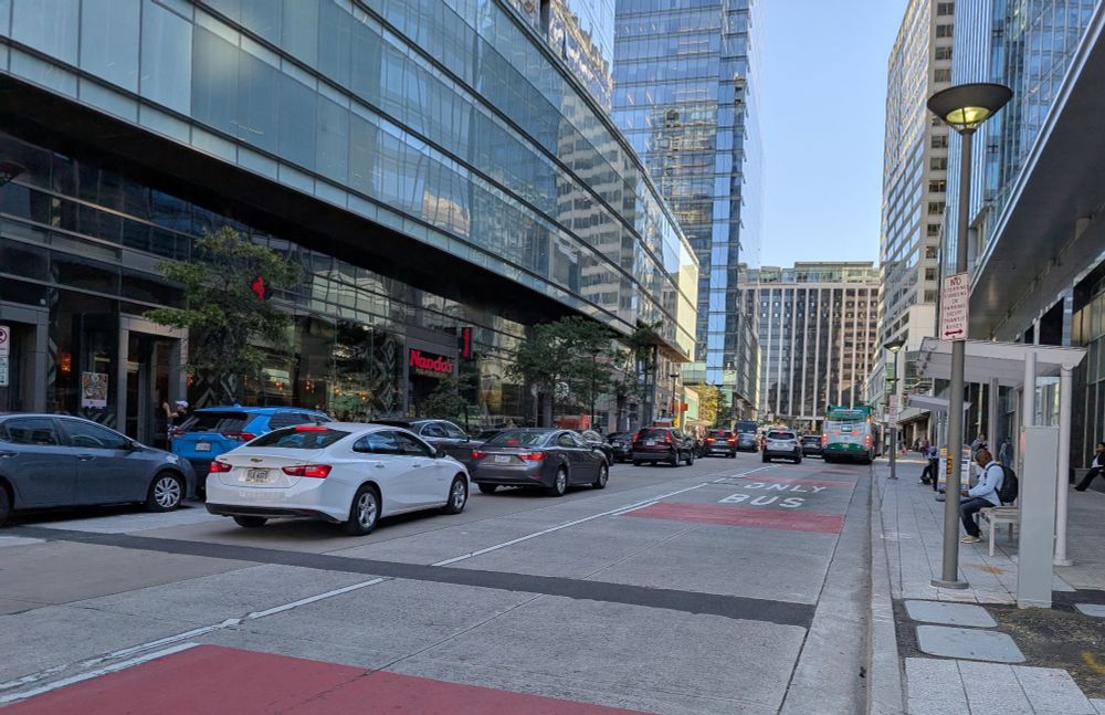 A line of some driving and some double parked cars on N Moore St