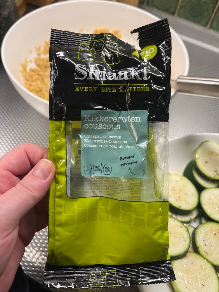 Een hand houdt een zakje Smaakt kikkererwten couscous vast. 