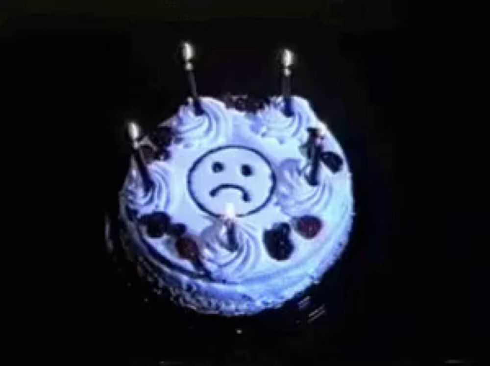 a birthday cake with a sad face on it and candles